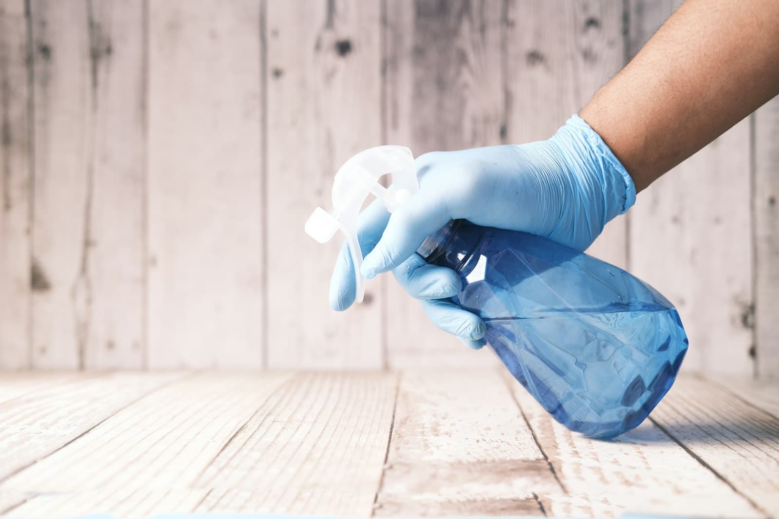Gloved hand holding a spray bottle over a surface